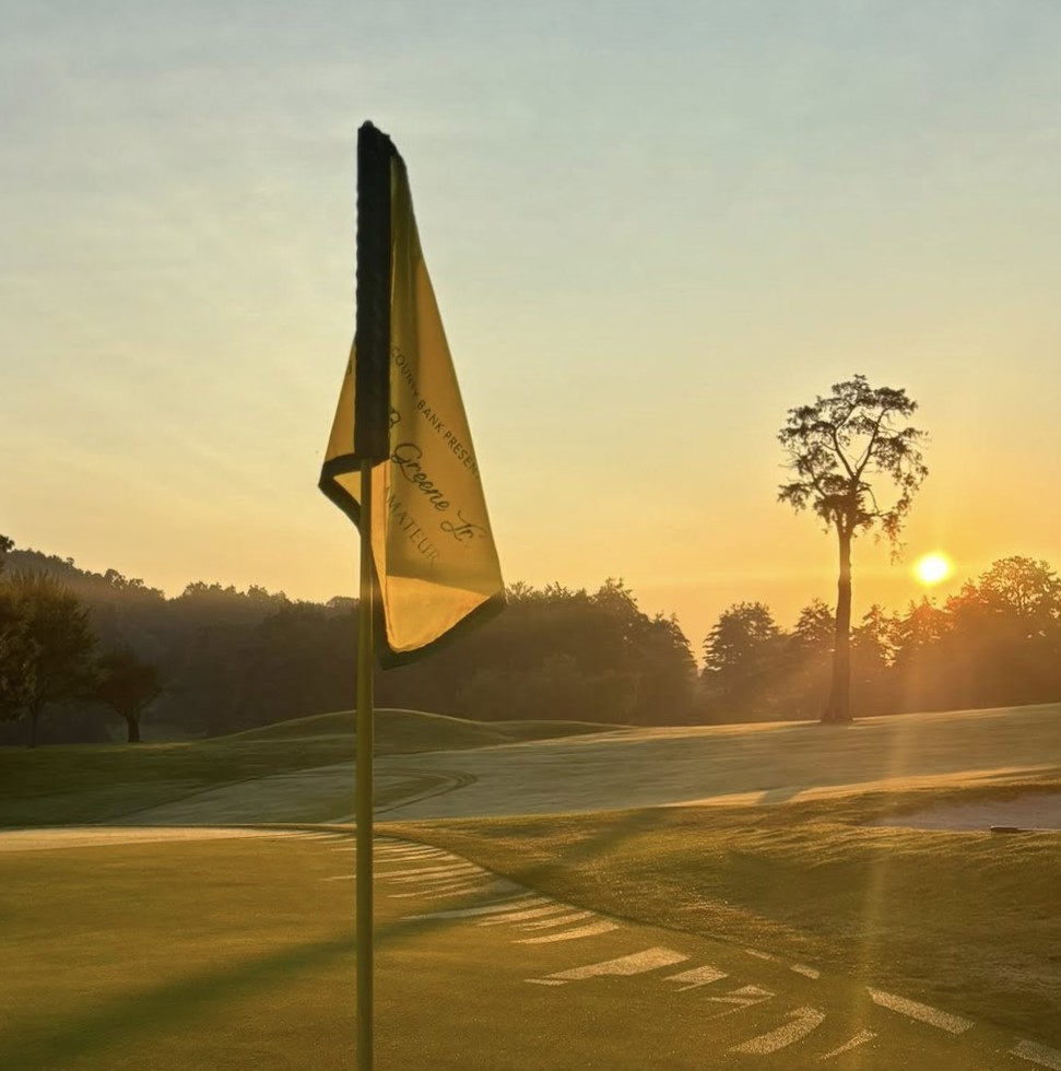 Flag pin at sunrise with the sun and rays visible in the distance.