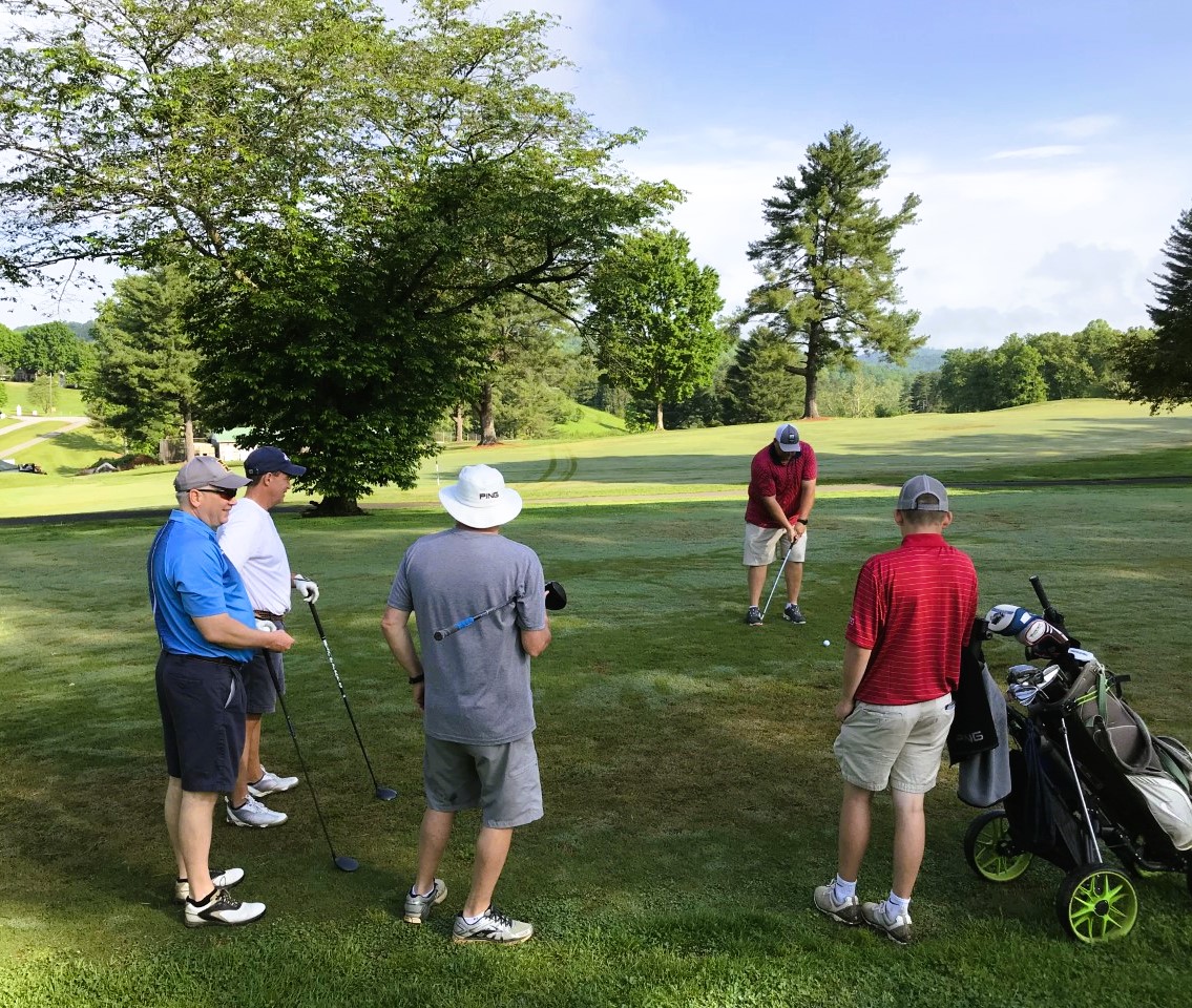 Four members watch as another golfer prepares his shot from the fairway.